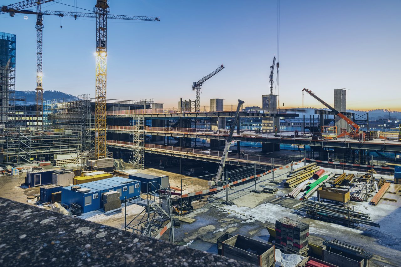 Construction site at blue hour — cranes over a floodlit structure